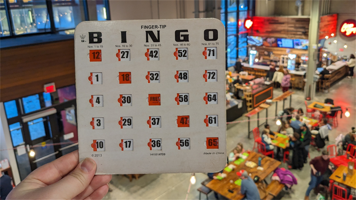 Hand holding up bingo card inside the Lenexa Public Market