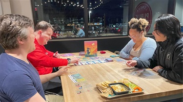 Group of four playing board game at table