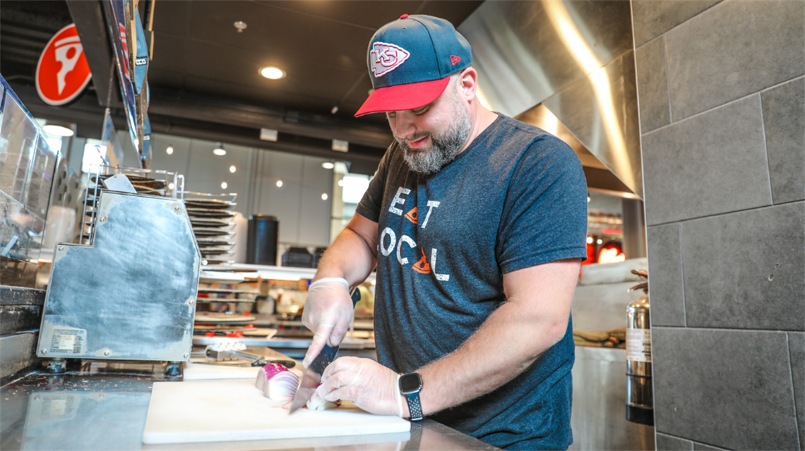 Chef/owner Chad Talbott dicing onions inside Topp'd Pizza + Salads' merchant stall