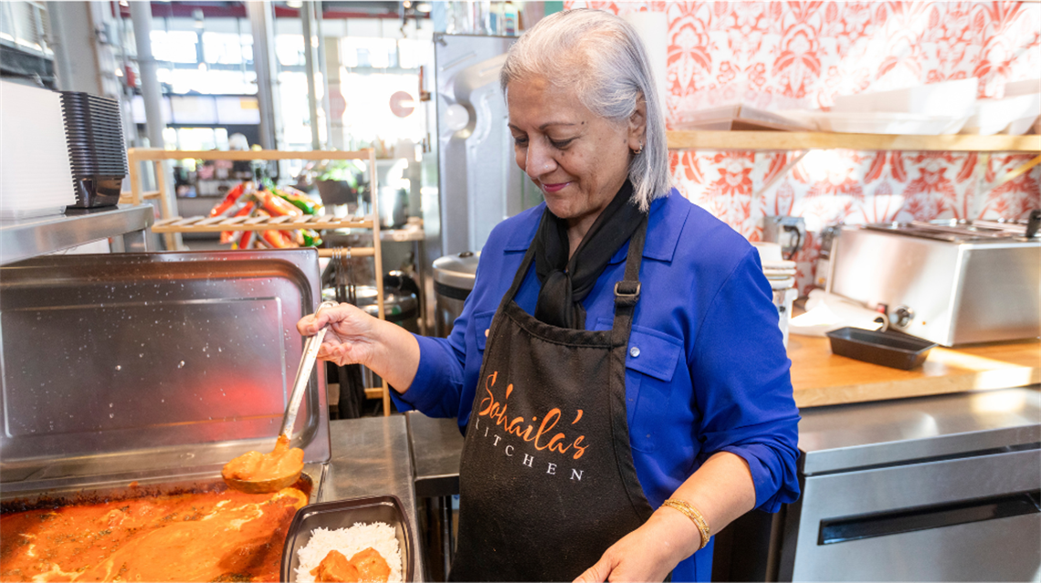 Sohaila of Sohaila's Kitchen serving a bowl of Butter Chicken inside her merchant stall