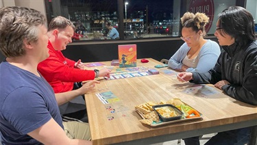 Four people at table playing a board game in The Kitchen